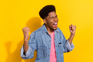 Photo of attractive lucky dark skin man wear jeans shirt smiling screaming rising fists space isolated yellow color background
