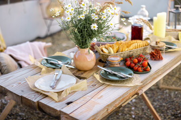 Beautifully served wooden table in natural boho style outdoors. Dining table decorated with field...