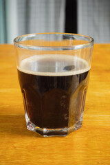 Hot black coffee in a clear glass is placed on yellow wooden table