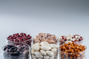 Six different varieties of beans in round glassware on a grey  background.