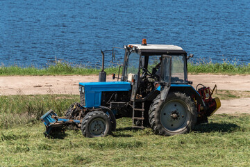 The tractor mows the grass on the river shore.