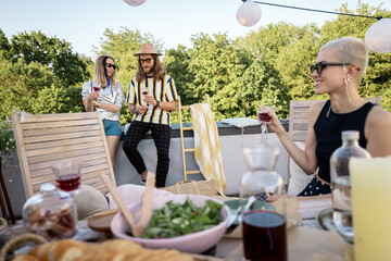 Group of young stylish people have a beautiful festive dinner outdoors. Friends talking and spending time together at picnic on a rooftop terrace