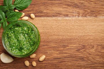 Basil pesto in bowl and ingredients on wooden background with copy space top view