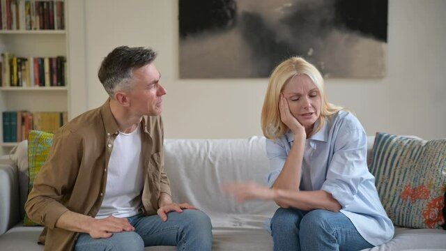 Misunderstanding, family quarrel. Upset, indignant gray-haired husband is emotionally talking and looking at his wife, gesturing with his hands, wife is upset because of a dialog, experiencing stress