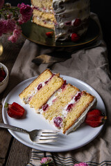 Piece of strawberry and mascarpone layered Victoria sponge cake  on white plate and pink roses on old wooden table .