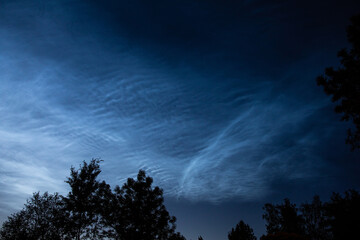 Noctilucent clouds or night shining clouds in midnight summer sky. Glowing white clouds in upper atmosphere where sun still shines on them.