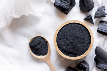 The black charcoal powder in the wooden cup was placed on a white cloth. - obrazy, fototapety, plakaty