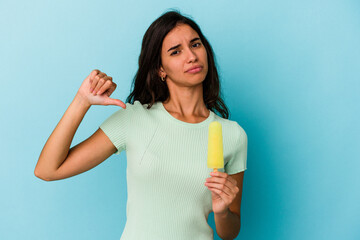 Young caucasian woman holding an ice cream isolated on blue background showing a dislike gesture, thumbs down. Disagreement concept.