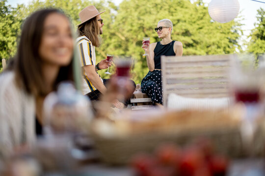 Two stylish carefree persons talk and drink wine at roof top terrace at countryside house. Friends hanging out at picnic outdoors