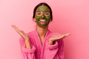 Young caucasian woman wearing a bathrobe and facial mask isolated on pink background receiving a pleasant surprise, excited and raising hands.