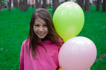 Fototapeta na wymiar pretty tween teenager brunette girl in pink holding colorful hot air balloons outdoors. party, birthday concept. summertime. happy children. hollidays, summer break