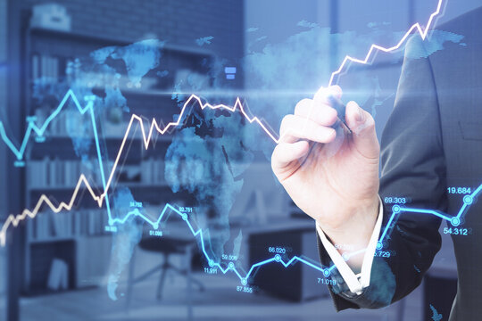 Businessman hand pointing at abstract glowing forex chart in blurry office interior. Economy and fund management concept. Double exposure.