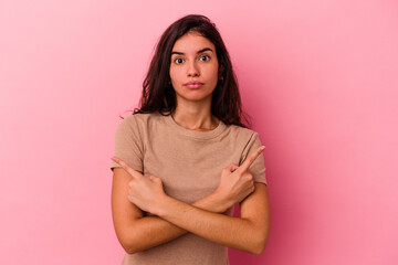 Fototapeta premium Young caucasian woman isolated on pink background points sideways, is trying to choose between two options.