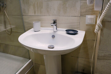 Silver metal shiny faucet water switch, ceramic sink in hotel home spa bathroom with tiles on wall. Bathroom modern luxury interior.