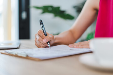 A cheerful middle-aged Asian businesswoman in relax casual dress working at home, checking email on computer laptop, writing on financial accounting document paper. Stock photo