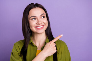 Photo of dreamy shiny young lady dressed green clothes smiling looking pointing finger empty space isolated purple color background