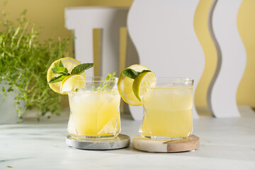 Two ice lemonade drinks in irregular glass with lime pieces and mint