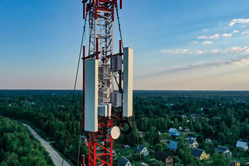 A cell tower against a blue sky and woodland, shooting from a drone.