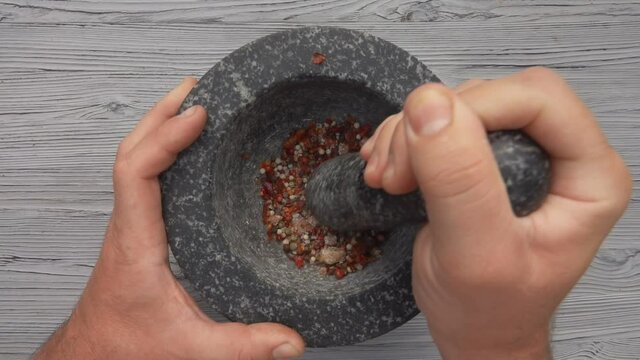 The top view of a pestle grinding spices, peppers and sea salt in a grey mortar