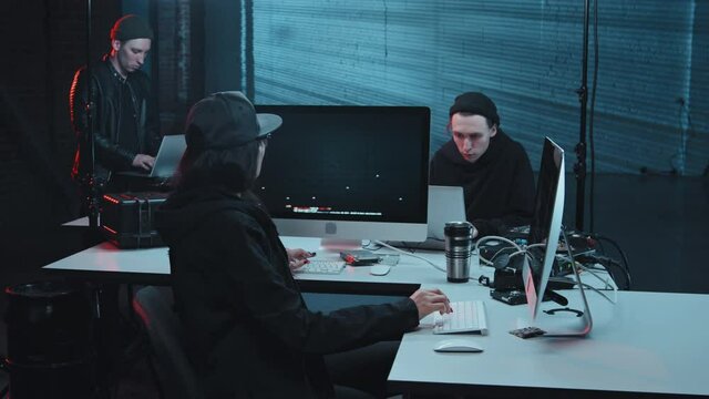 Slowmo tracking shot of male and female hackers coding on computers and laptops in dark secret hideout