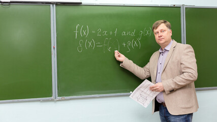 A male school math teacher at the blackboard explains the solution of the problem.