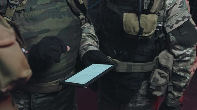 Handheld slowmo tracking shot of team of SWAT officers looking at tablet and planning mission