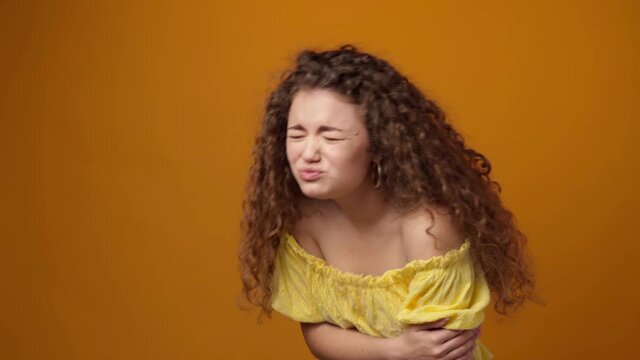 Young woman suffering stomach ache against yellow background in studio