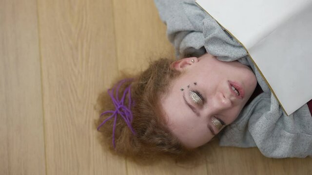 Close-up top view of young hipster woman sleeping on the floor with book. Tired exhausted Caucasian millennial taking a nap enjoying hobby at home indoors. Lifestyle and resting