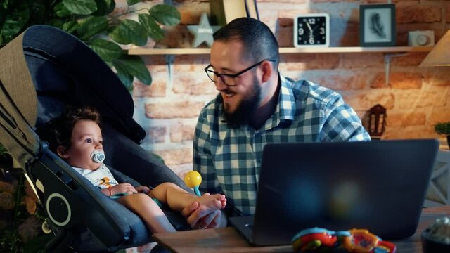Young programmer takes care of his son in a wheelchair while working from home on a laptop at night
