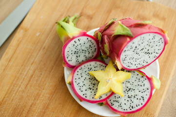 Slices of dragon fruit or pitaya with white pulp and black seeds on white plate with one slice of starfruit or averrhoa carambola. Exotic fruits, healthy eating concept