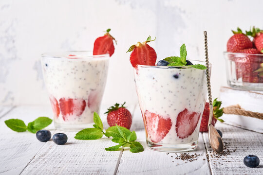 Two strawberry chia seeds layered smoothie or milkshake with strawberry and blueberry mint in glass on light grey background. Summer and healthy dieting drinks, vegetarian food concept.