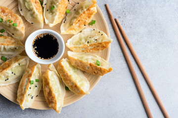 Gyoza or jiaozi, chinese fried dumplings served with soy sauce and sesame seeds on bamboo plate,...
