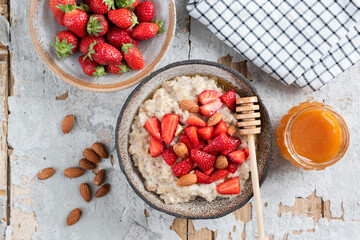 Breakfast oatmeal with strawberries and honey in bowl on old concrete table, overhead view