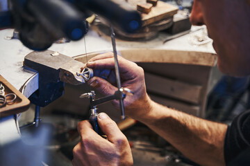 Male jeweler cutting silver item with saw frame