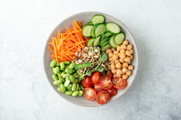Fototapeta na wymiar Overhead view of vegan buddha bowl salad with vegetables, microgreen sprouts, chickpeas and edamame beans on grey concrete background