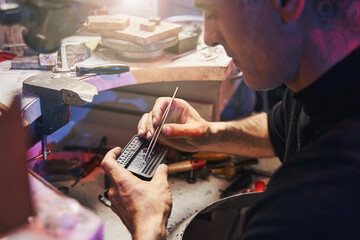 Cautious goldsmith is taking diamond with tweezers