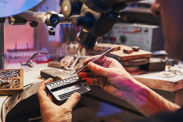 Male jewelry maker lifting diamond with tweezers