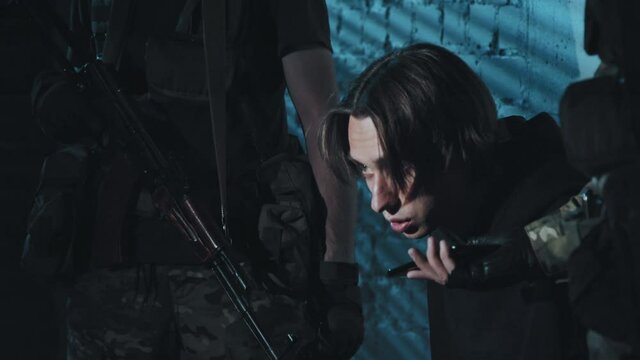 Handheld slowmo shot of unrecognizable armed terrorists holding man hostage He is talking into mobile phone and listing their demands