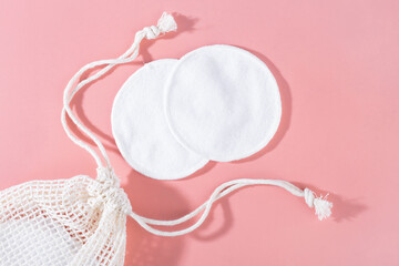 organic cotton pads with string bag on pink background. Zero waste, reusable, eco, makeup remover. shadows, hard light, flat lay