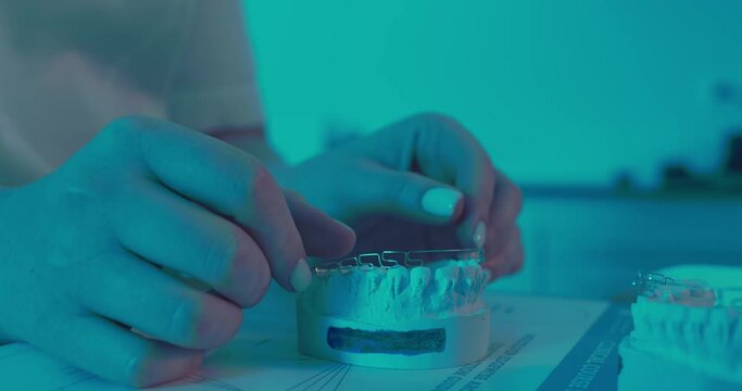 A close-up ceramic model of a lower jaw and a female orthodontist is putting on it a multiloop edgewise archwire.
