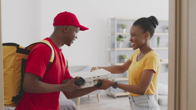 Fast food delivery service. Happy young african american woman paying for pizza with contactless smartphone system