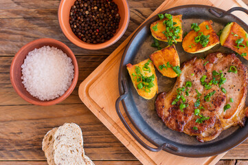Roasted pork steaks in frying pan from neck meat with potato. wooden background.