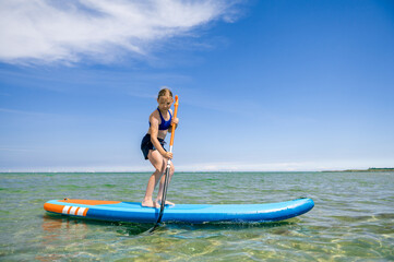 Cute little girl ecercise paddling on SUP board in sea on sunny day while summer holidays