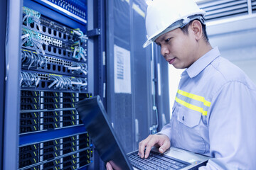 Network administrator holding laptop in hand working Configuration with core switch on rack cabinet...