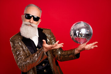 Photo of young positive old man hold hands disco ball wear sunglass magic isolated on red color background - obrazy, fototapety, plakaty