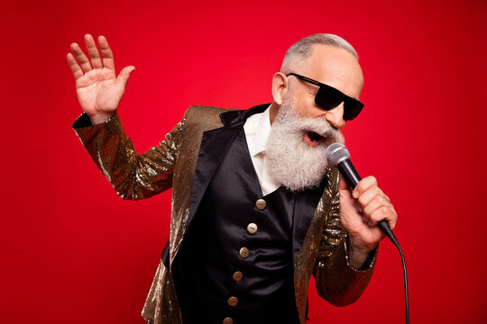 Photo Of Singing Beard Aged Magician Man Sing In Mic Wear Gold Jacket Eyewear Isolated On Red Color Background