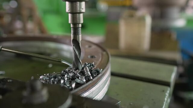 A metal drill makes holes in a metal product on an industrial drilling machine with shavings. Metalworking industry. The machine drills a hole.