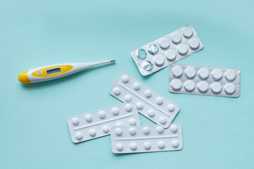 The medical thermometer and pills in blister packs on blue background. Disease prevention and treatment concept. Top view.