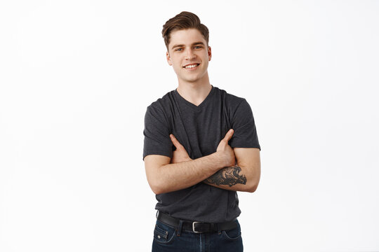 Modern guy with white smile. Handsome young man cross arms on chest, looks happy and confident, standing in casual clothes against white background