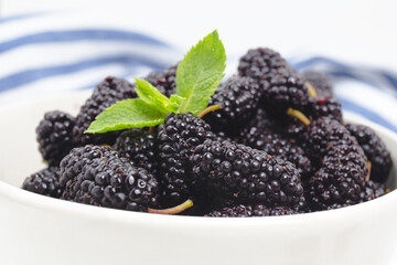 White bowl full of ripe black mulberries. Summer fresh mulberry fruit. Healthy berries with vitamin C and antioxidants. Close-up, macro. fresh mulberry bowl. Mulberry background.